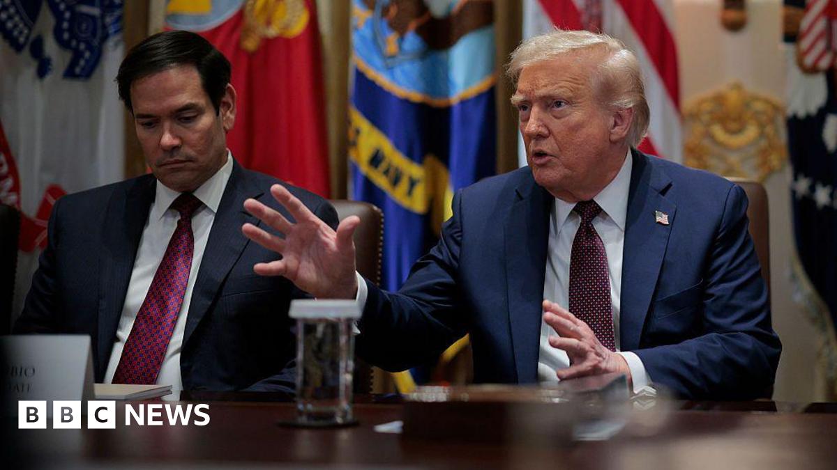 Donald Trump speaks at a table. US Secretary of State Marco Rubio sits next to him.