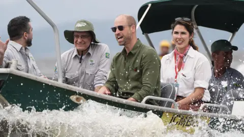 PA Media Five people on a boat, with William in the centre, wearing dark sunglasses. On his right are two men, on his left is a woman and a another man. In the forefront of the picture is sea spray as the boat moves through the water