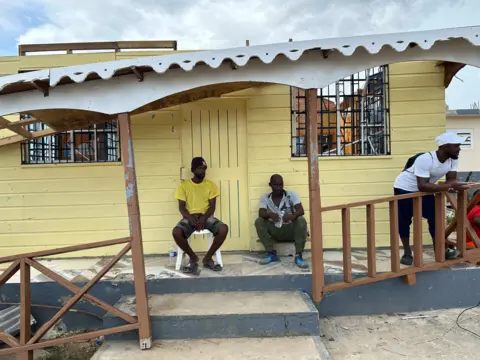 Brandon Drenon / BBC Two men are seated beneath a building half blown away by the storm