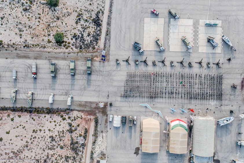 A large group of soldiers standing in formation carrying various flags and surrounded by weapons and war planes