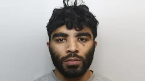 South Yorkshire Police A police mugshot of Hassan Jhangur. He has dark facial hair and dark, slightly curly hair.