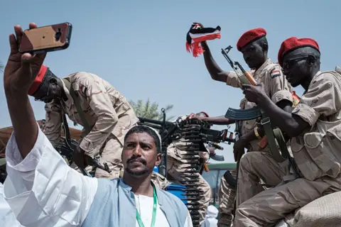 AFP via Getty Images A Sudanese man takes a selfie with members of the Rapid Support Forces (RSF), in uniforms and with guns, in the capital Khartoum on 18 June 2019