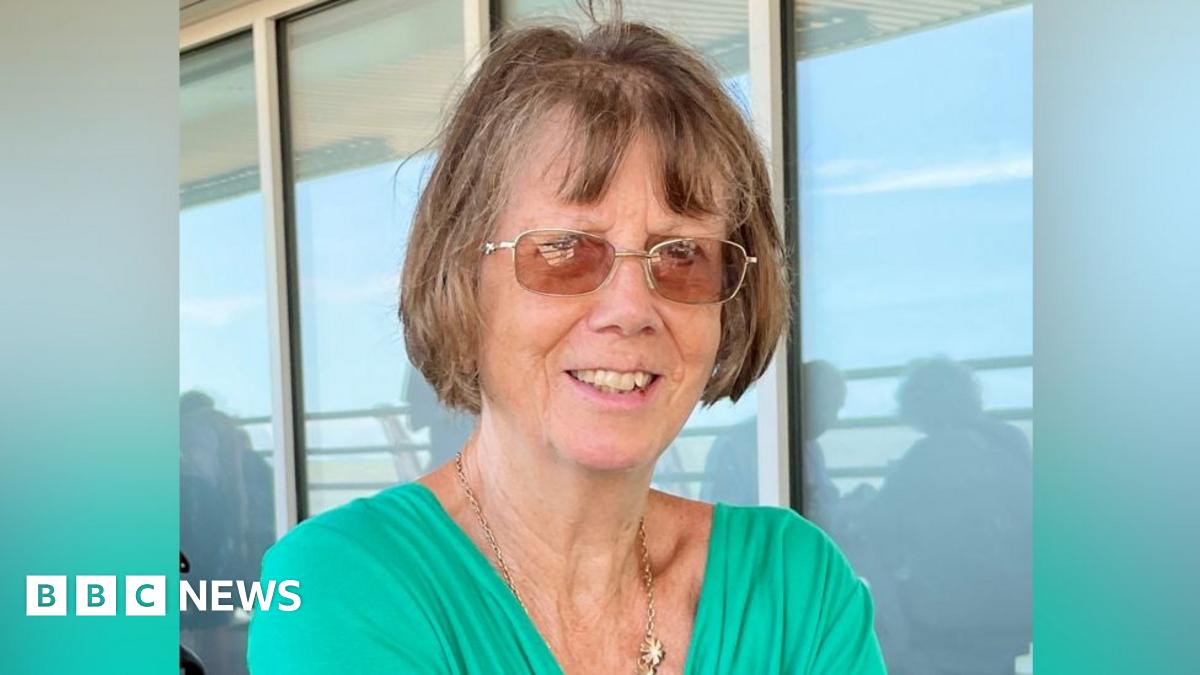 Christine Murton is in the middle of the image looking towards the camera. She has short brown hair and is wearing glasses and a green T-shirt.