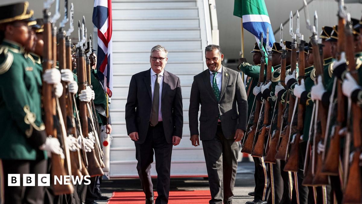 Keir Starmer lands in South Africa and is greeted by a South African official . He walks past people in uniform holding rifles