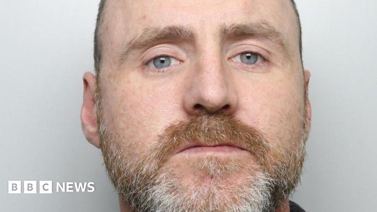 A man staring straight ahead. He has a ginger and grey-coloured beard with very short hair.