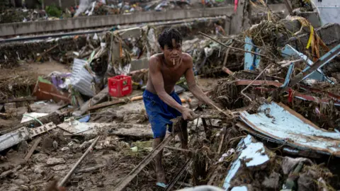 Reuters A man can be seen wearing shorts and flip flops, picking through a scene of destruction caused by Typhoon Kalmaegi in Talisay, Cebu, Philippines, on 5 November 2025
