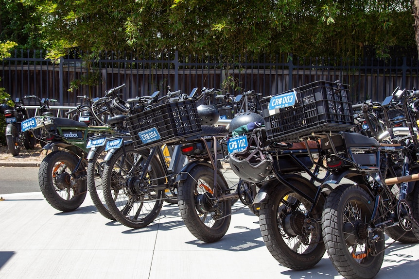 a row of e-bikes leaning against bike racks outdoors