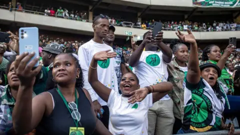 Getty Images MK Party supporters take pictures and wave at a political rally in a stadium.