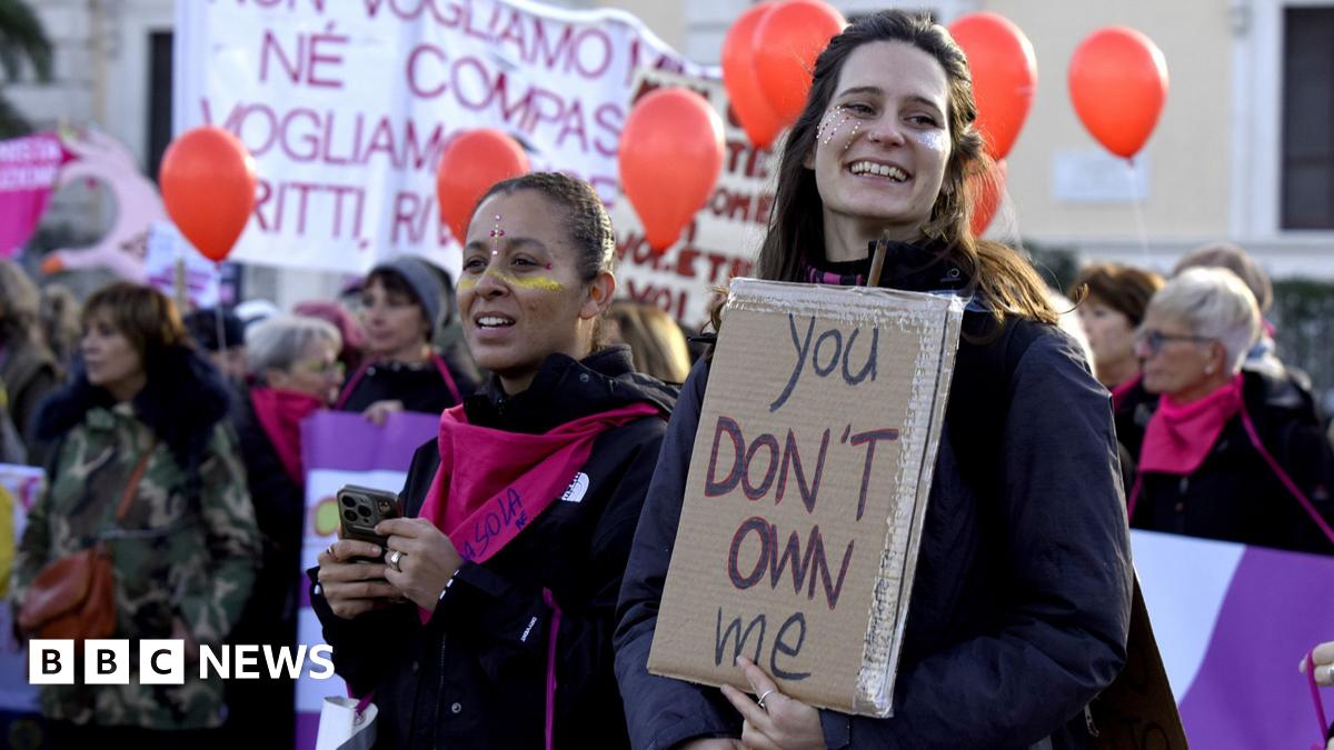 Two people stand during a protest, one smiles and the other looks away from camera holding a placard that reads 'you don't own me', with other demonstrators in the background holding orange balloons, in Rome on 22 November.