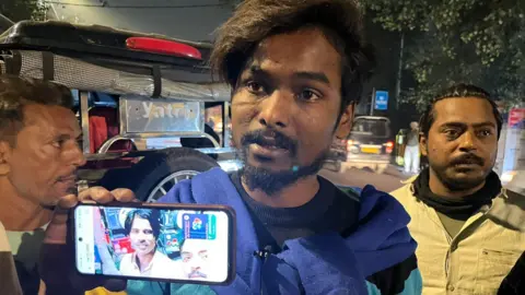 BBC Man holds up a mobile phone showing the photo of his missing brother after an explosion in Delhi's Red Fort area killed at least eight people and injured many.