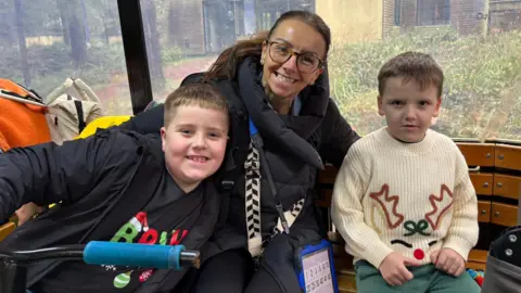 SUPPLIED Claire Naylor sat in between sons Jaxon and MJ on a bench