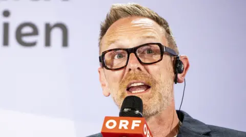 Getty Images Martin Green, with spiky blond hair and dark thick-rimmed glasses, speaks into a microphone labelled ORF 