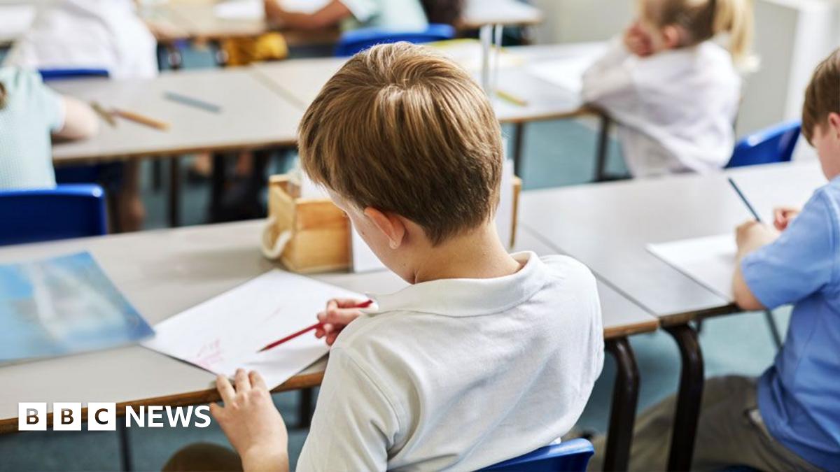 Schoolchildren in classroom holding pencils and writing in exercise books