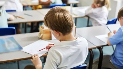 Getty Images Schoolchildren in classroom holding pencils and writing in exercise books 
