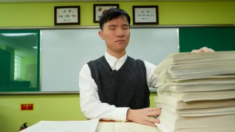 BBC/Hosu Lee Han Dong-hyun from Seoul School for the Blind reads a braille practice exam, with the standard printed version placed beside it