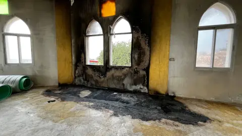 The blackened floor and wall of the Hamida Mosque where a fire has burned. You can see patches where the paint has burnt away