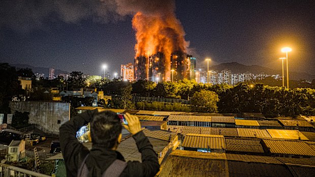 An onlooker takes photos as a major fire engulfs several apartment blocks at the Wang Fuk Court residential estate.