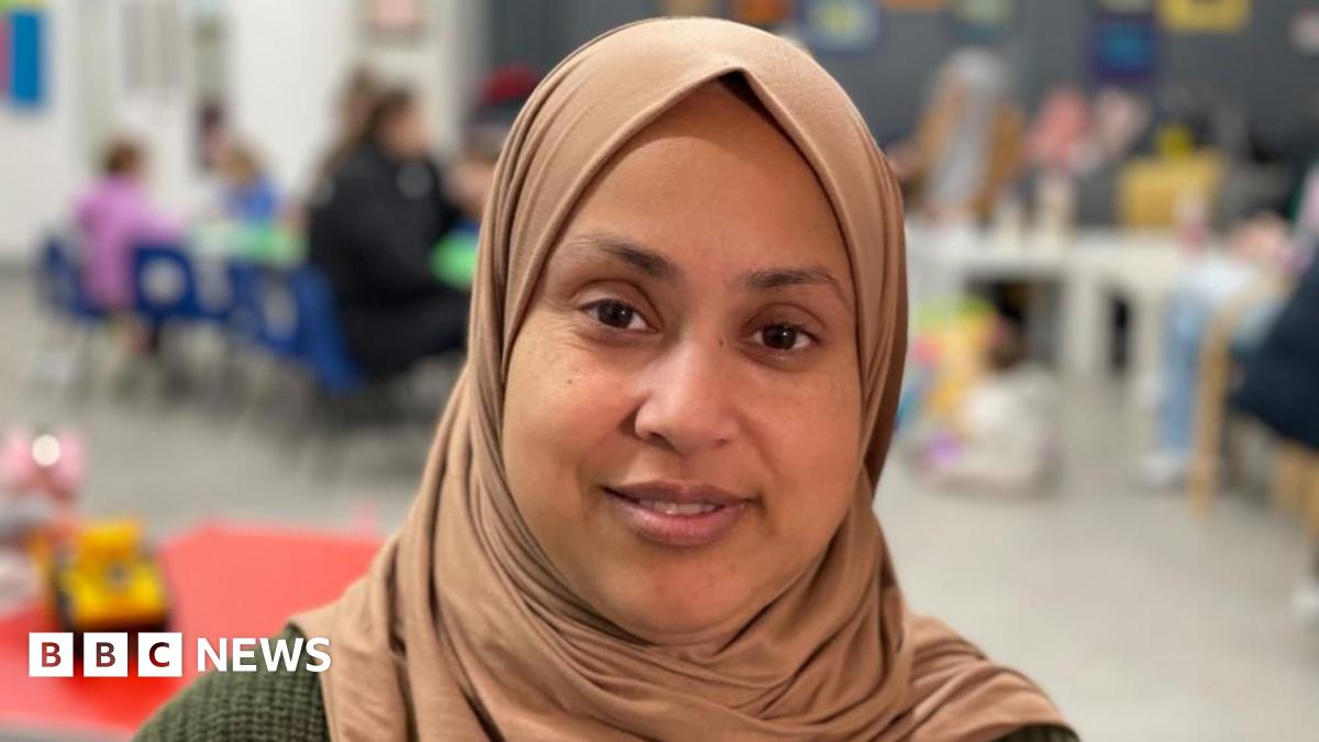 A woman in a brown headscarf and green top smiles at the camera.
