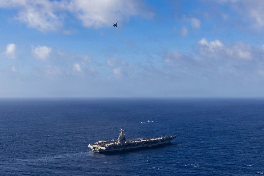 A F/A-18E Super Hornet fighter aircraft flies over the USS Gerald R. Ford on November 5, 2025.