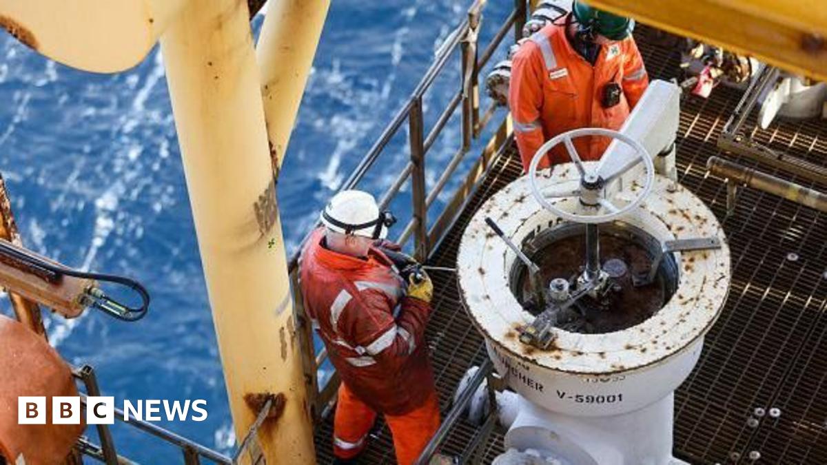 Offshore worker Phil Perry, who has a bald head and is wearing a black T-shirt, is smiling at the  camera. He has tattoos on arms.