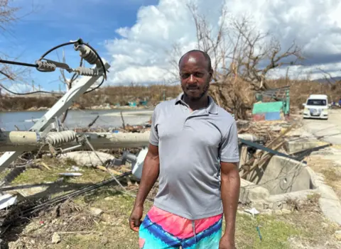 Brandon Drenon / BBC Robert Morris stands in front of his fishing village that was flattened by Hurricane Melissa