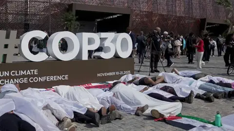 Getty Images People are lying on the ground in front a COP30 sign, covered in white sheets as part of a protest at the talks in Brazil