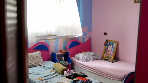 BBC/Goktay Koraltan A child's bedroom is seen with blue and pink walls, two beds and a large framed image of a little girl