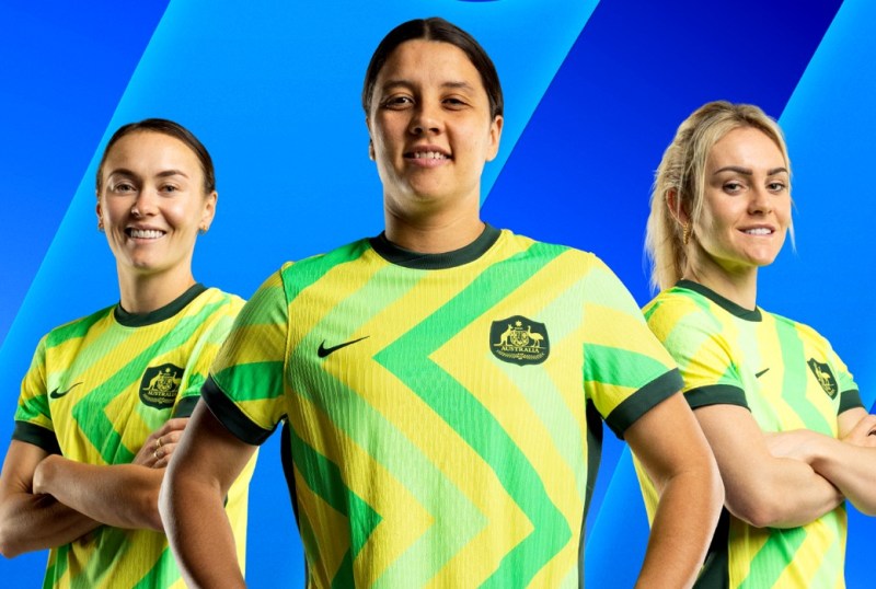 Australian women's soccer team members posing in their vibrant green and gold jerseys against a blue background, showcasing team spirit and pride.