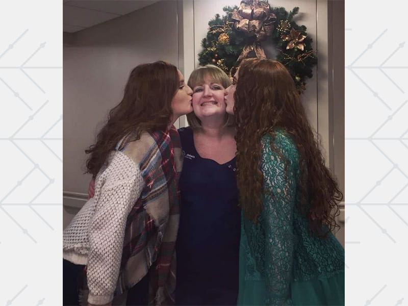 Paige (left) and Mallory on either side of their mother, Natalie Daugherty, kissing her on the cheeks