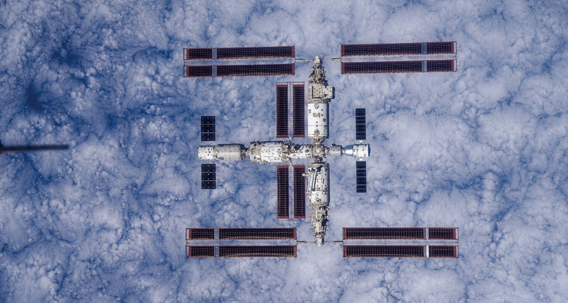 a large T-shaped space station is seen from above with Earth below it