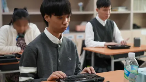 BBC/Hosu Lee Students sit at their desks with their hands placed on braille display devices