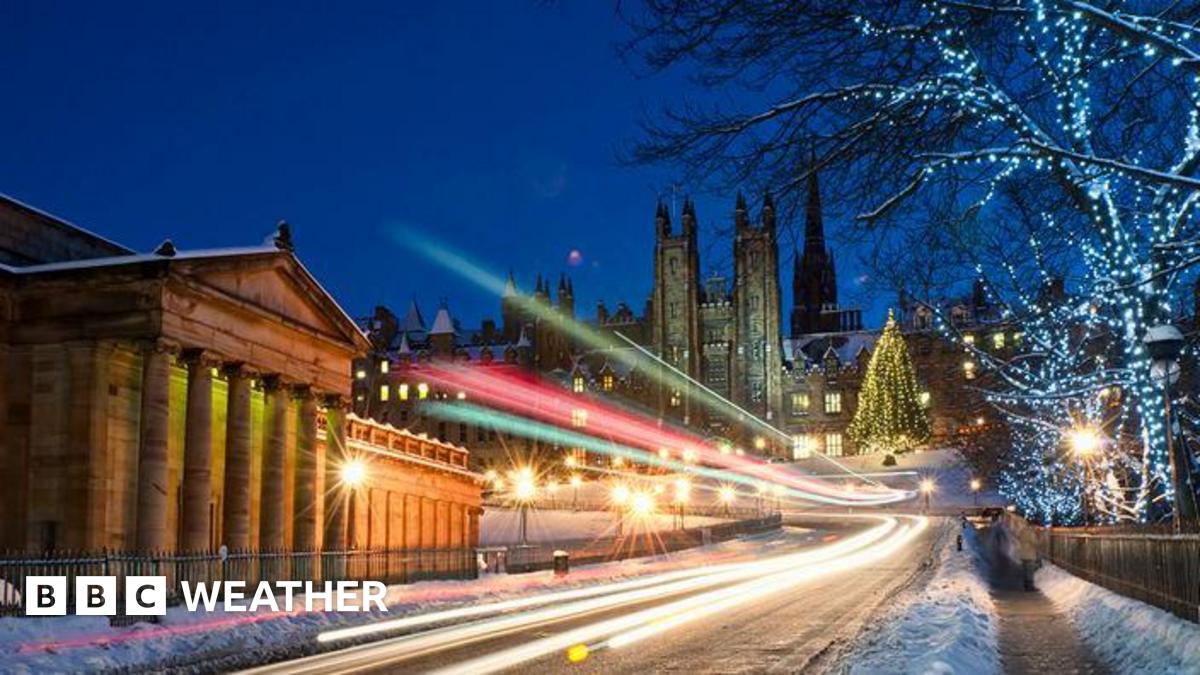 Light trails from traffic moving along a snowy road in central Edinburgh, with an illuminated Christmas tree visible in the distance.