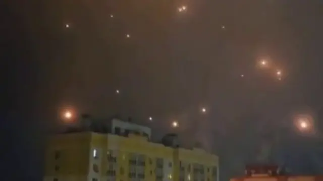Burning orange embers - likely to be debris from the air attack - fall around a yellow and white tower block in Oryol
