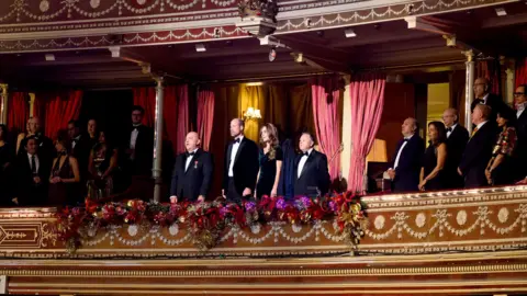 ITV/Shutterstock (left to right) Giles Cooper OBE, Their Royal Highnesses Prince William and Catherine Princess of Wales and Phil Dale in the royal box at the Royal Albert Hall for the Royal Variety Performance 2025, in London on 19 November 2025.