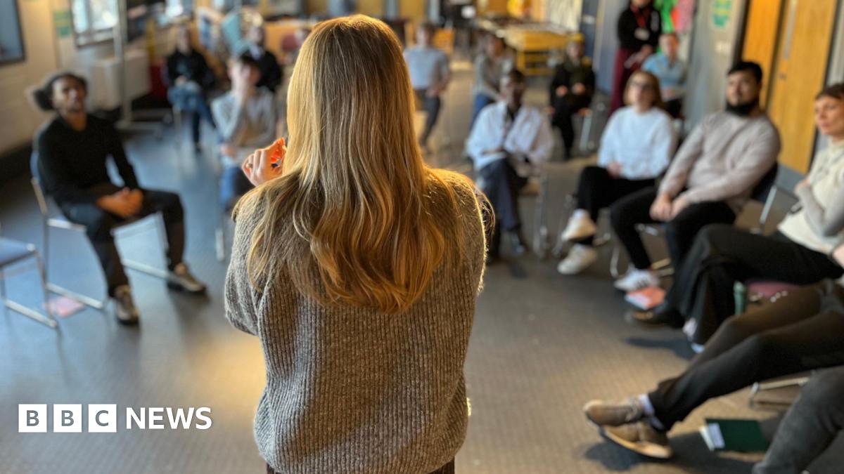 A group of young people who are not in education, employment or training sit in a semicircle during a group coaching session on employability skills.