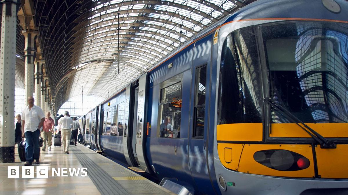 Paul Costelloe has receding grey hair. He is wearing a bright pink, blue and green scarf and a blue jacket.