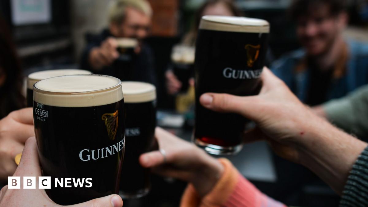 A crowd of people holding Guinness pints in a cheers motion.