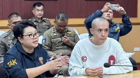 EPA-EFE/REX/Shutterstock Wang Xing sitting on the right of a table in a white sweater and shaved head. Beside him is a person in navy uniform. Sitting behind are police officers in their uniforms.