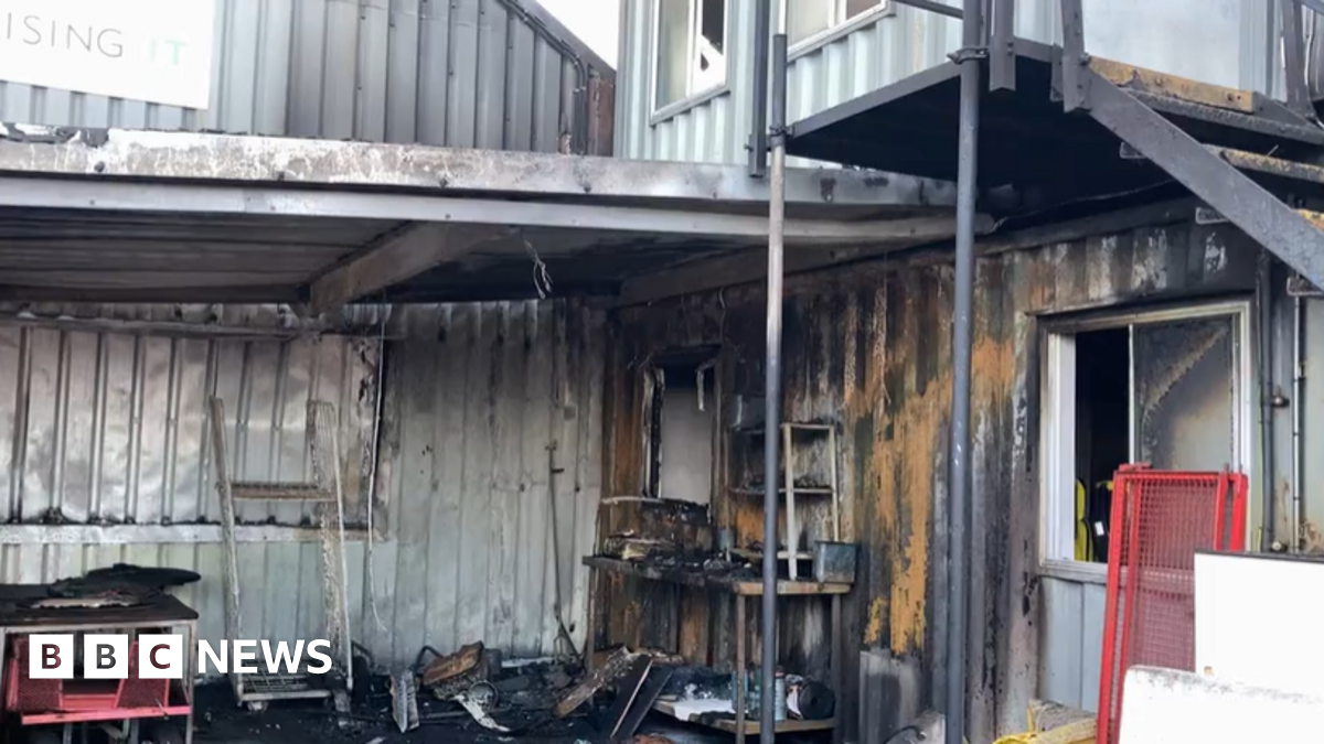 A fire damaged portacabin. The metal is burnt and there are items on the floor black from the smoke.