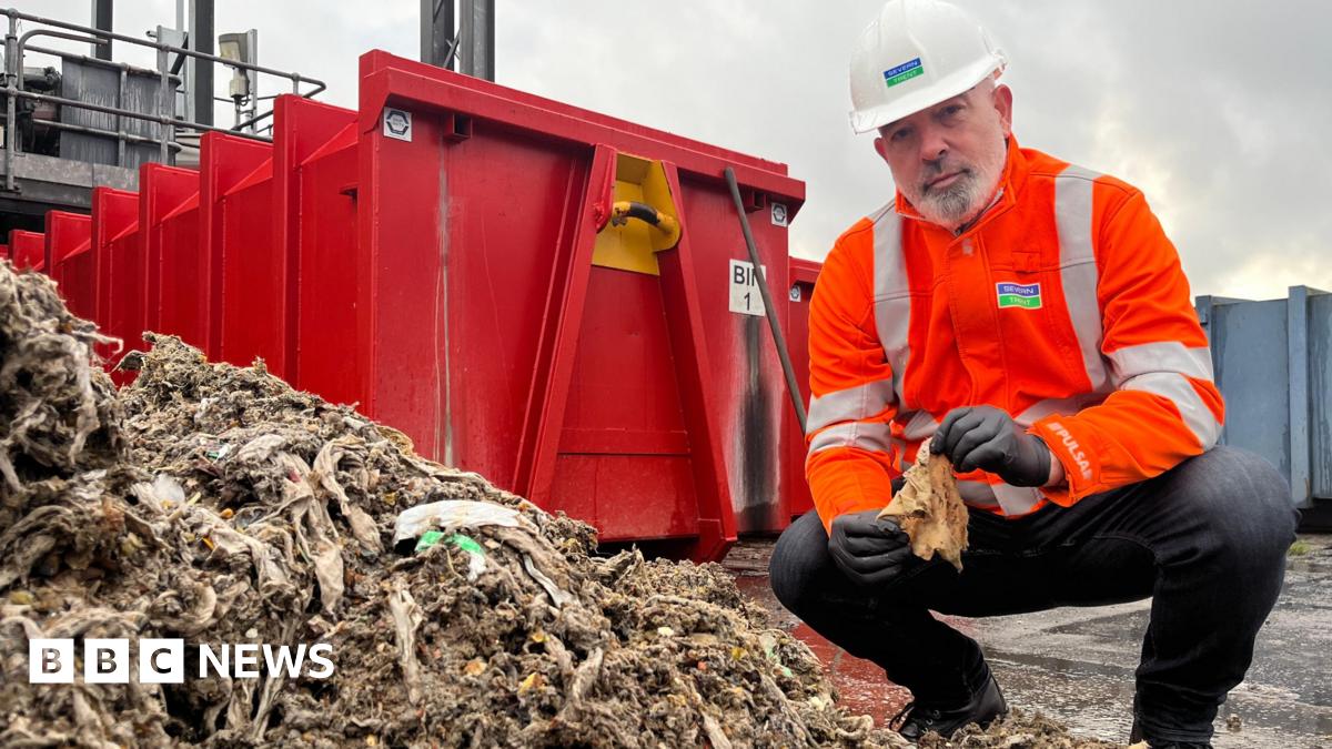 An employee of Severn Trent holds a soiled wet wipe in front of a pile of wet wipes.