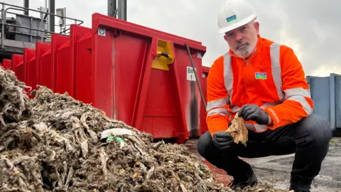 Jonah Fisher/BBC An employee of Severn Trent holds a soiled wet wipe in front of a pile of wet wipes. 