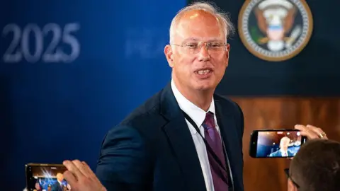 Bloomberg via Getty Images Kirill Dmitriev in a blue jacket poses for photographers in Alaska with whispy silver hair and transparent glasses