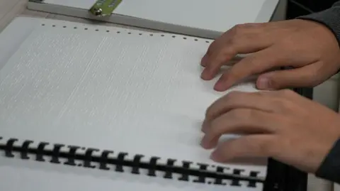 BBC/Hosu Lee Two hands on a braille practice booklet for the Suneung exam
