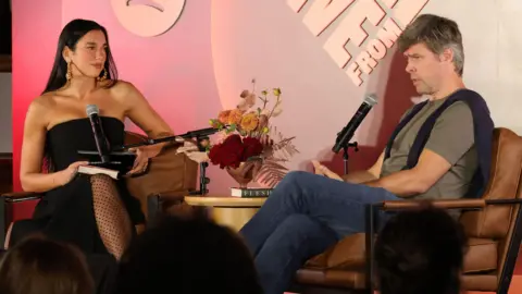 Getty Images Dua Lipa and David Szalay sitting on a stage in front of microphones