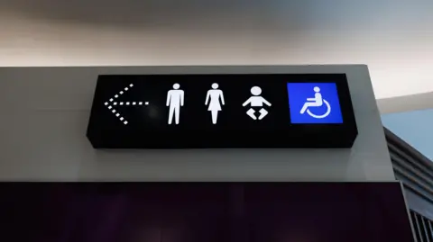 Getty Images A photo shows a toilet sign with male, female, child and disabled icons