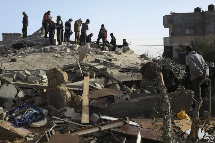 A group of people stand atop a pile of rubble