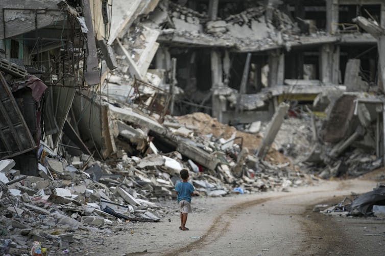A small child walks beside destroyed buildings and mounds of rubble