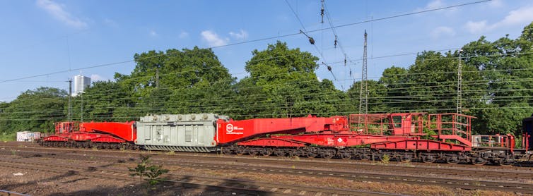 A massive railcar carries a large metal box.