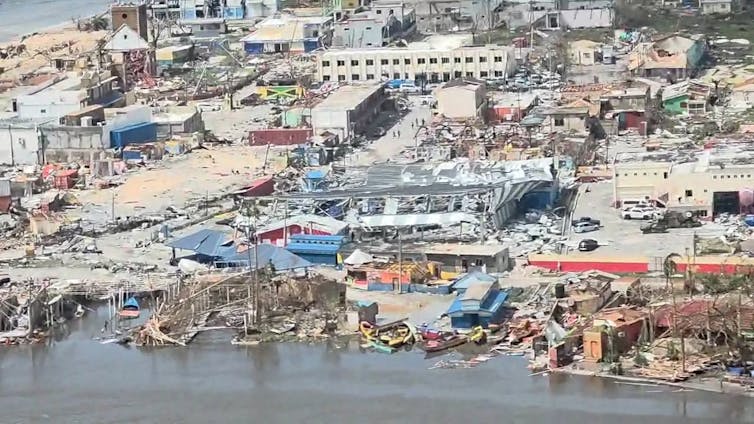 An aerial view of a city damaged by the hurricane. Mud is in the streets and buildings have lost roofs and walls.