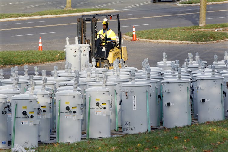 A person drives a forklift near a group of large metal canisters.